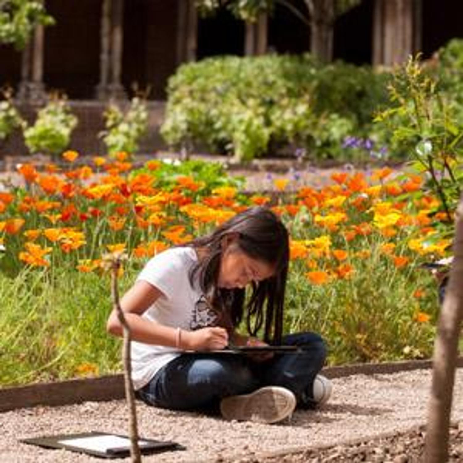 photo - une petite fille dessine assise par terre dans le jardin du cloître